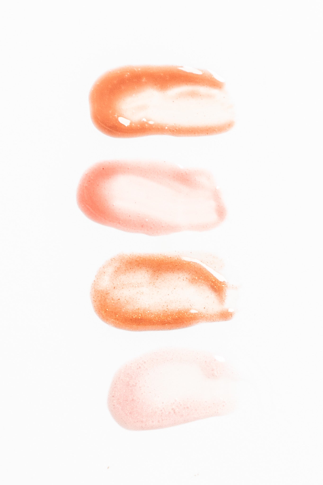Three swatches of a peach-colored lip gloss on a white background