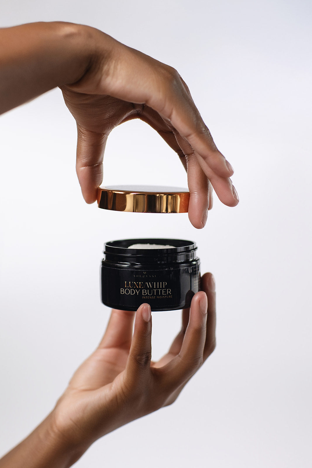Black body butter jar with gold lid held by a hand against a white background