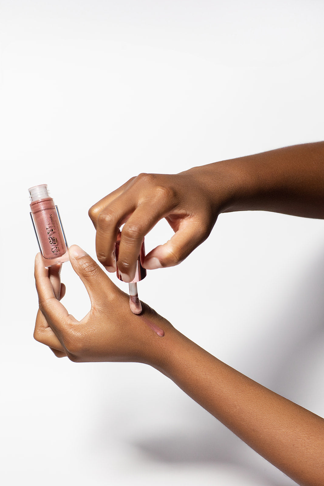 Two hands holding a small bottle of pink lip gloss against a white background