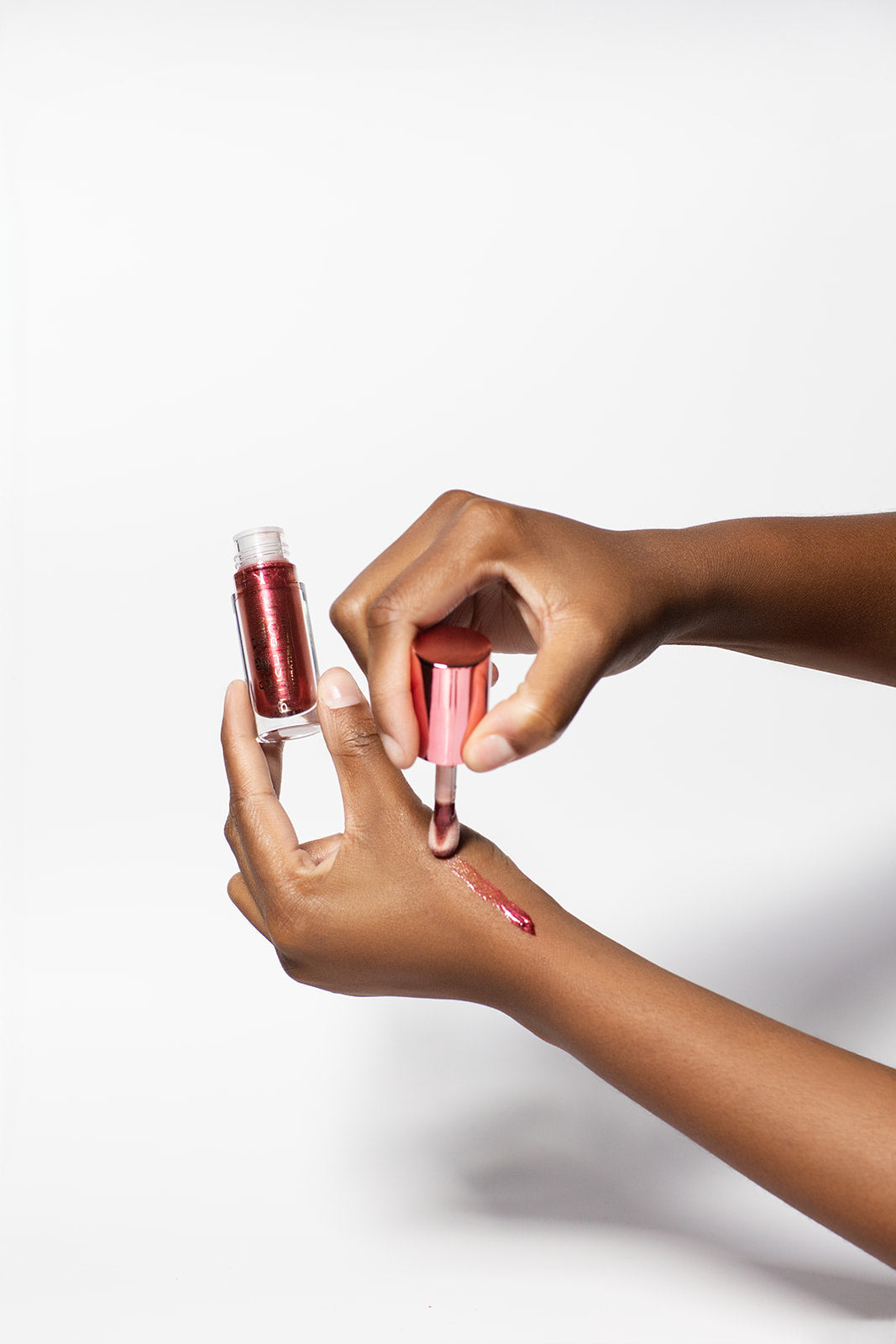 Person applying red lip gloss to their hand against a white background