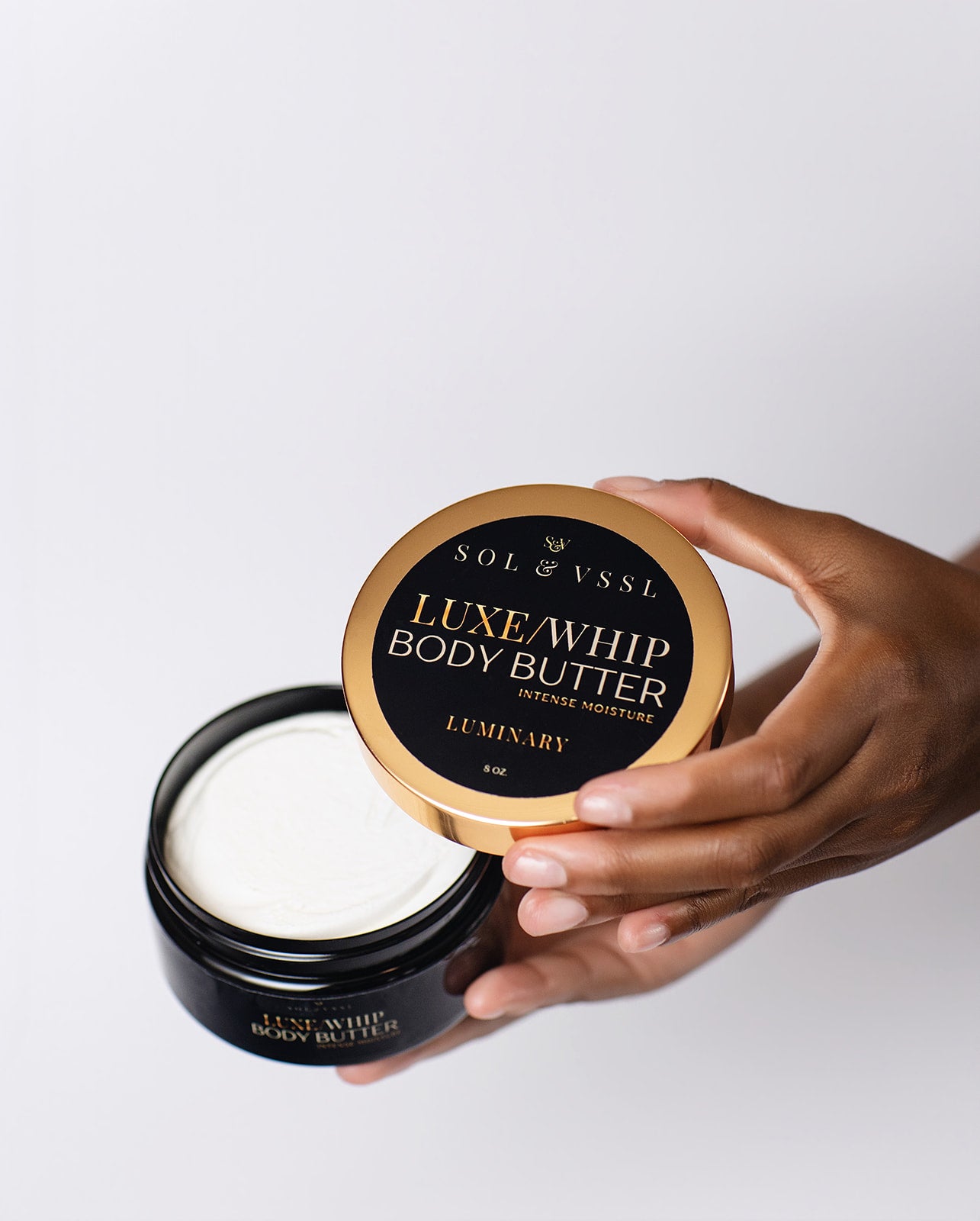 Hand holding a jar of Luxe Whip Body Butter with a white background