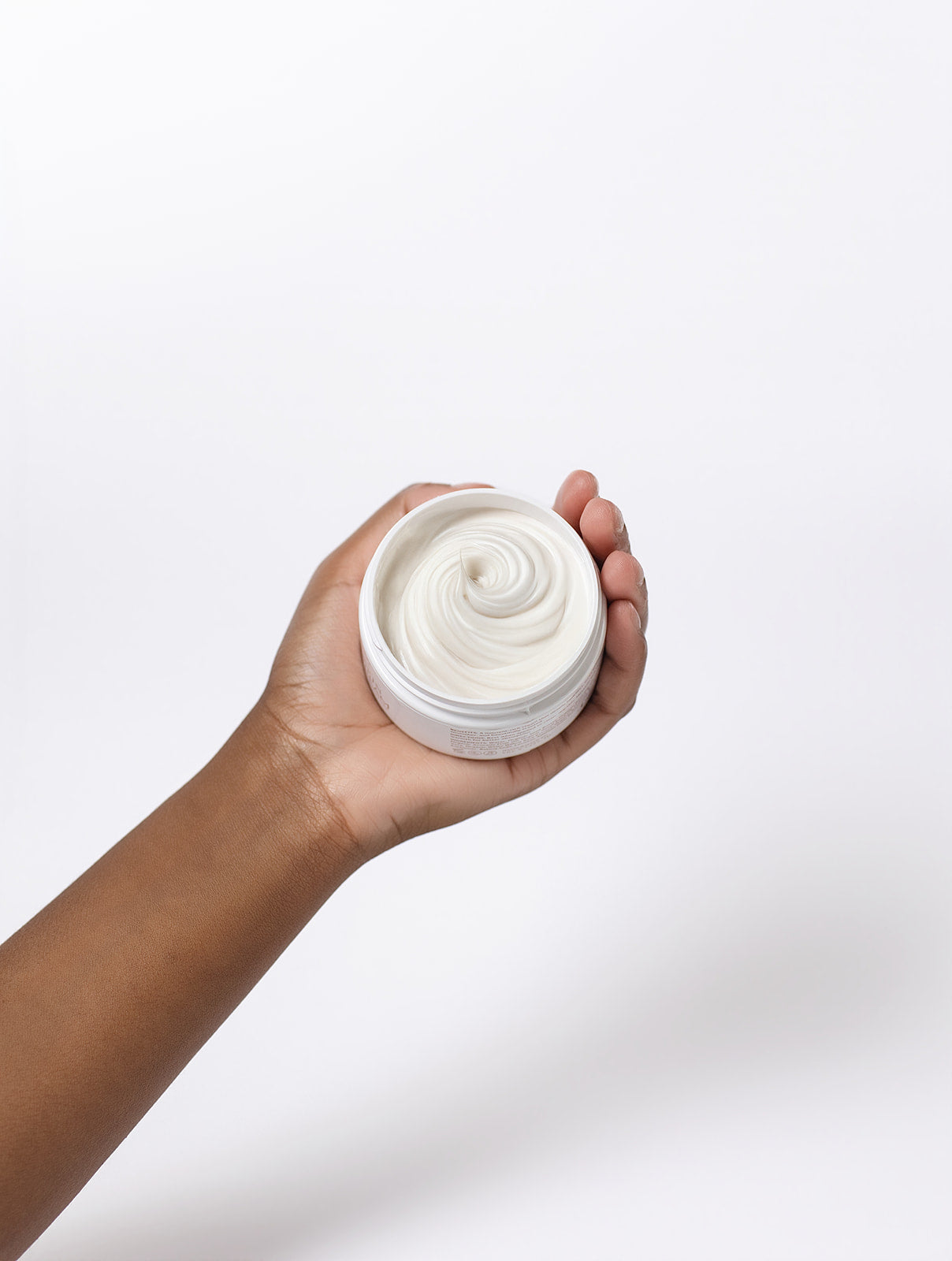 Hand holding a white jar of cream against a light gray background
