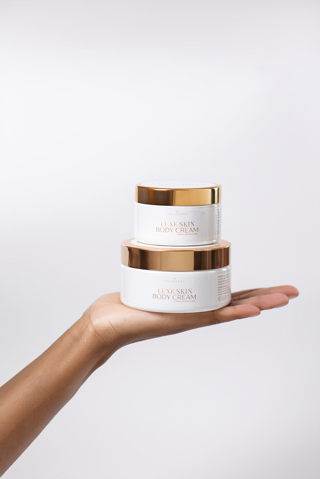 Two skincare cream jars held in a hand against a light background