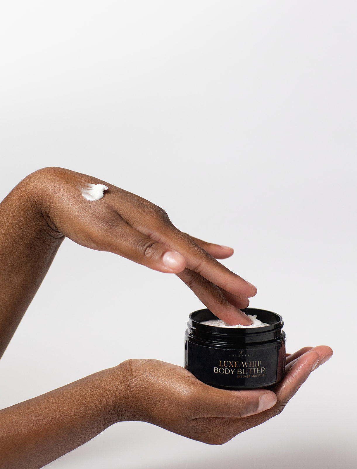 Person applying Luxe Whip Body Butter to their hand with a white background