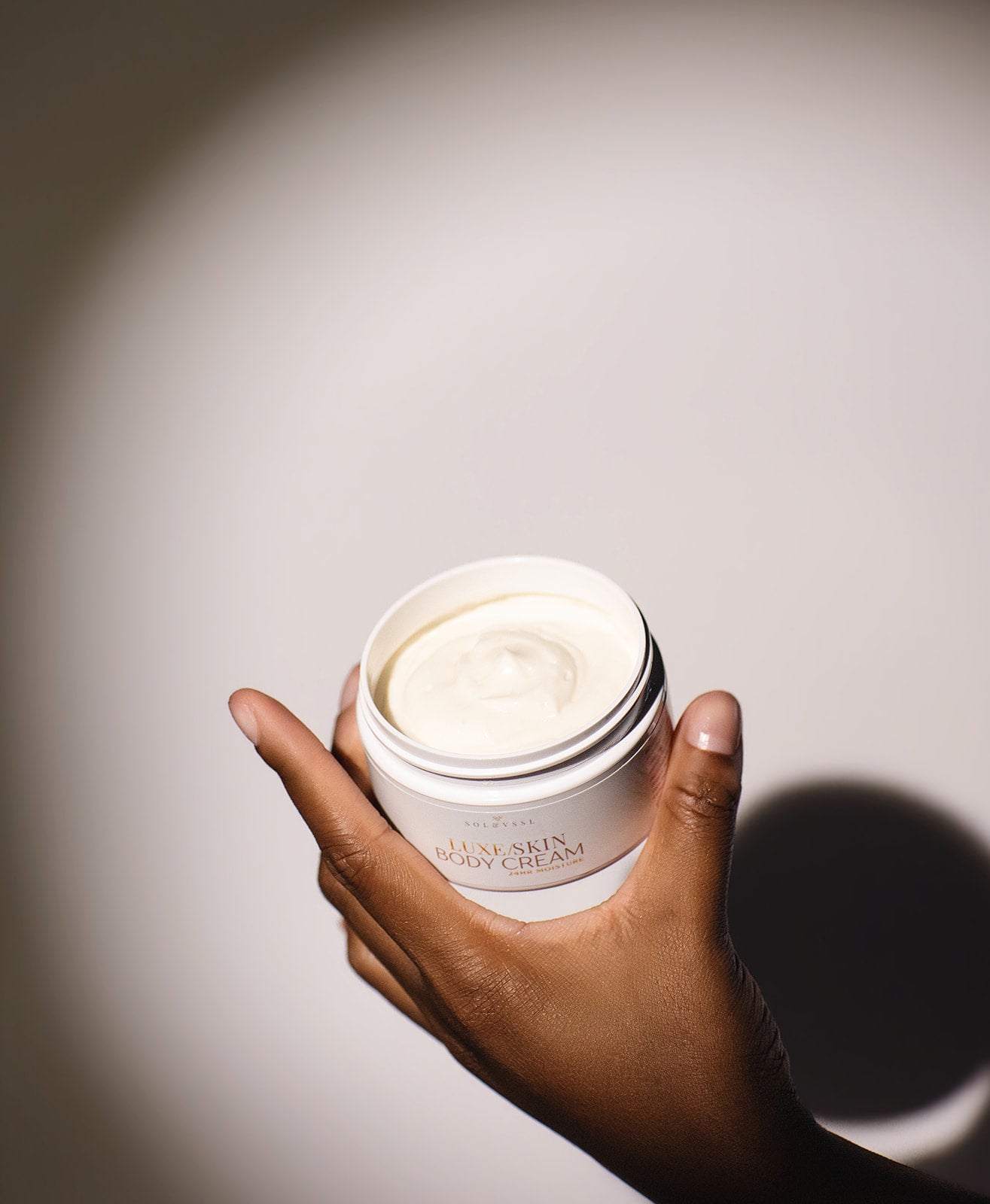 Hand holding a jar of cream with a soft light on a neutral background
